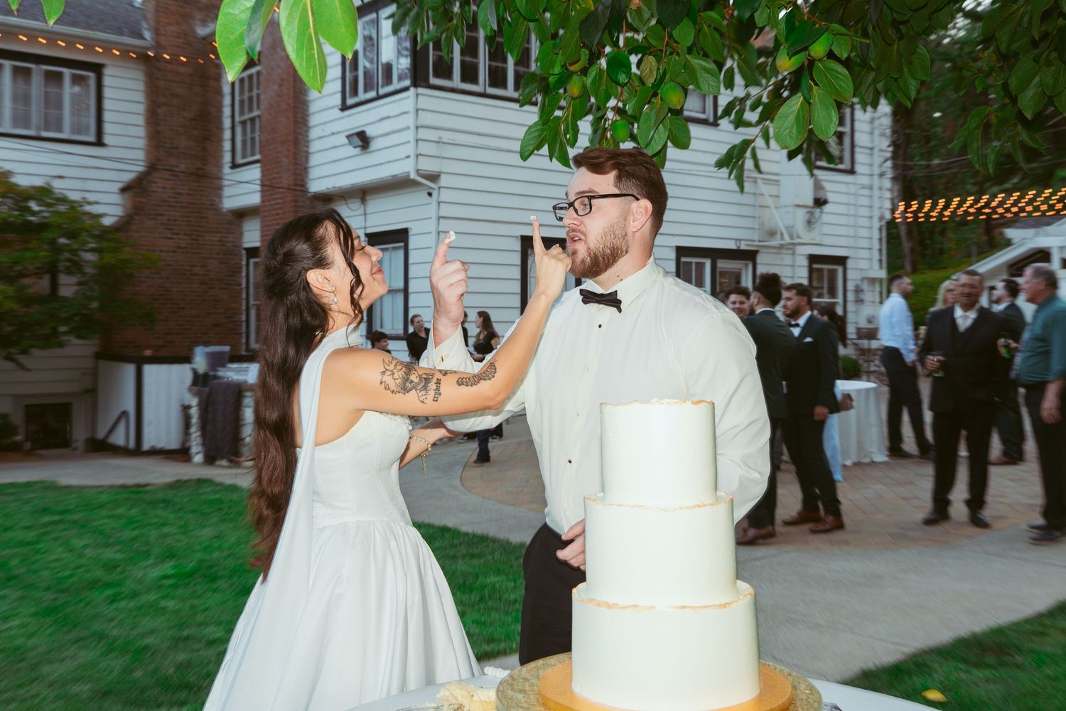 Wedding couple cutting their white tiered cake at outdoor reception.