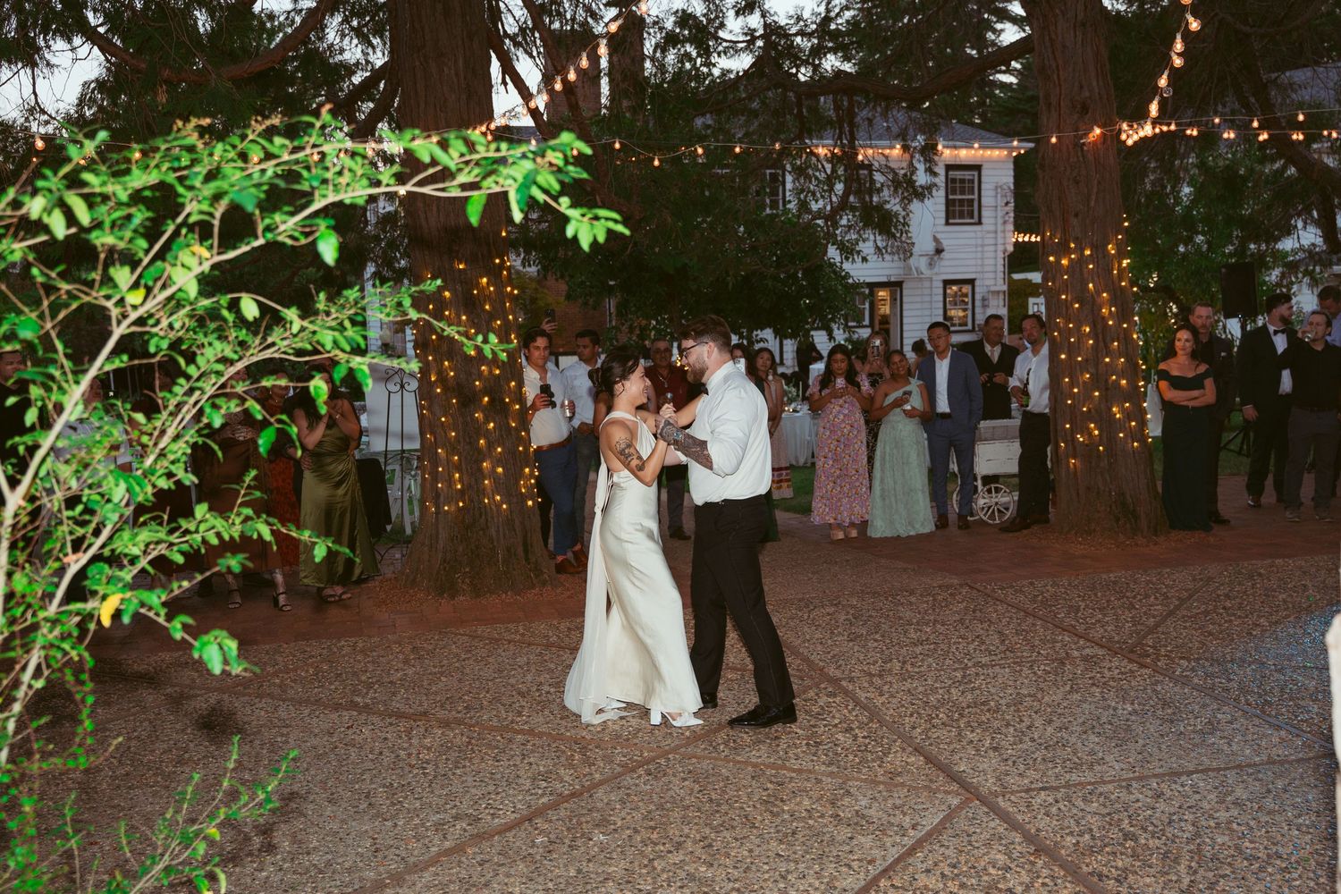 Couples sharing romantic dances on an outdoor dance floor under twinkling lights and tree branches.