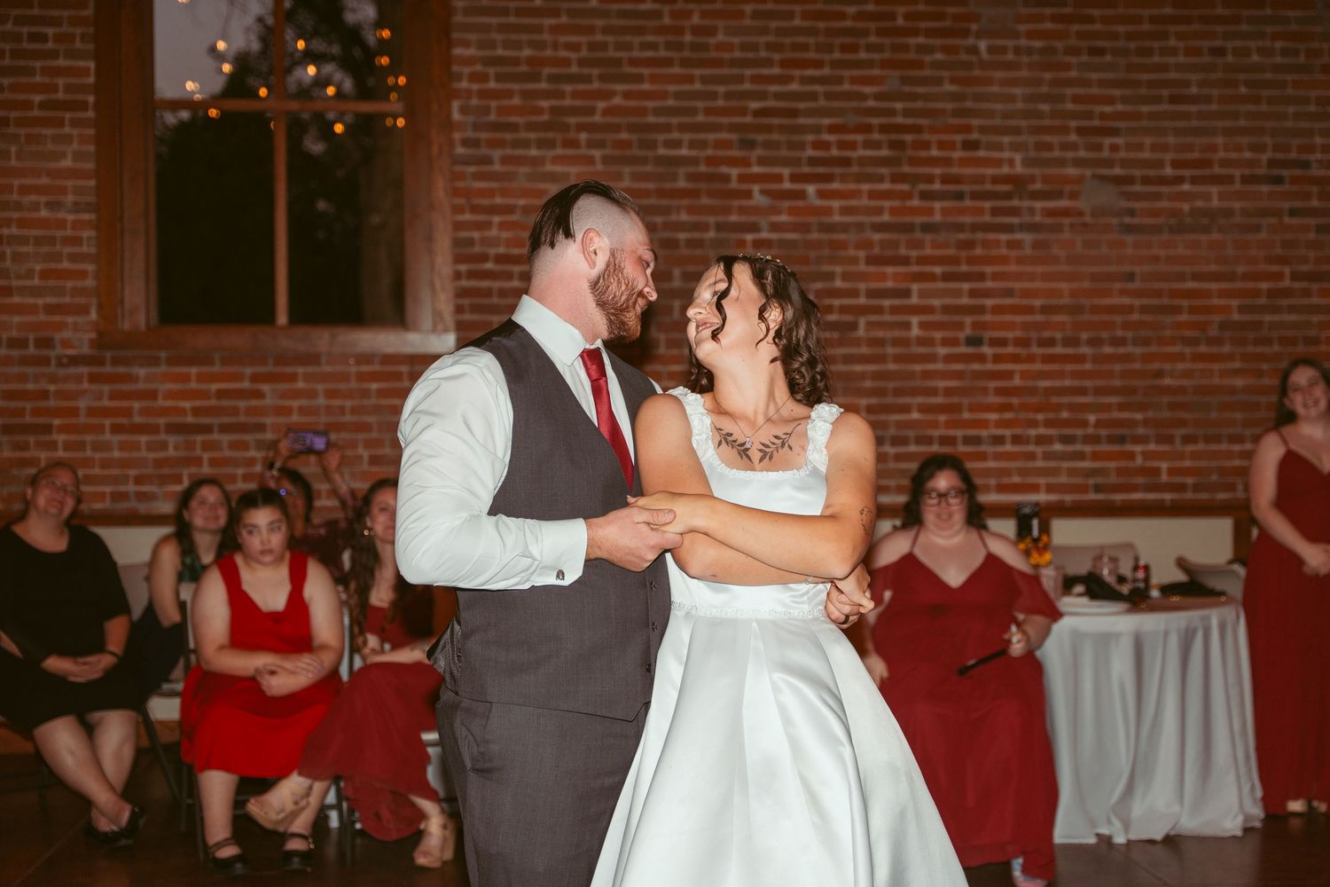 Wedding dance floor moment in rustic brick venue with romantic lighting.