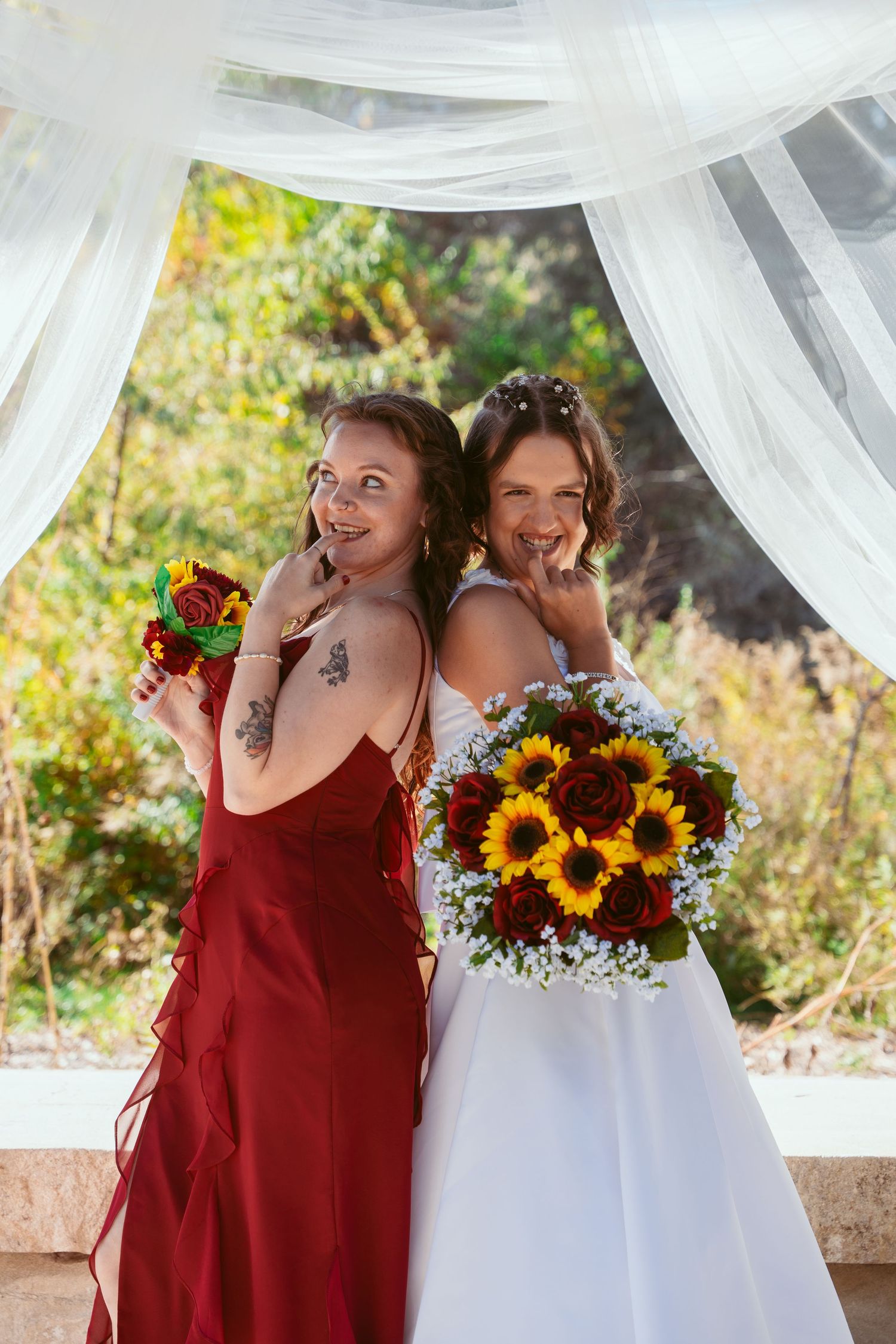 Wedding celebration with burgundy and white attire under draped outdoor pavilion.