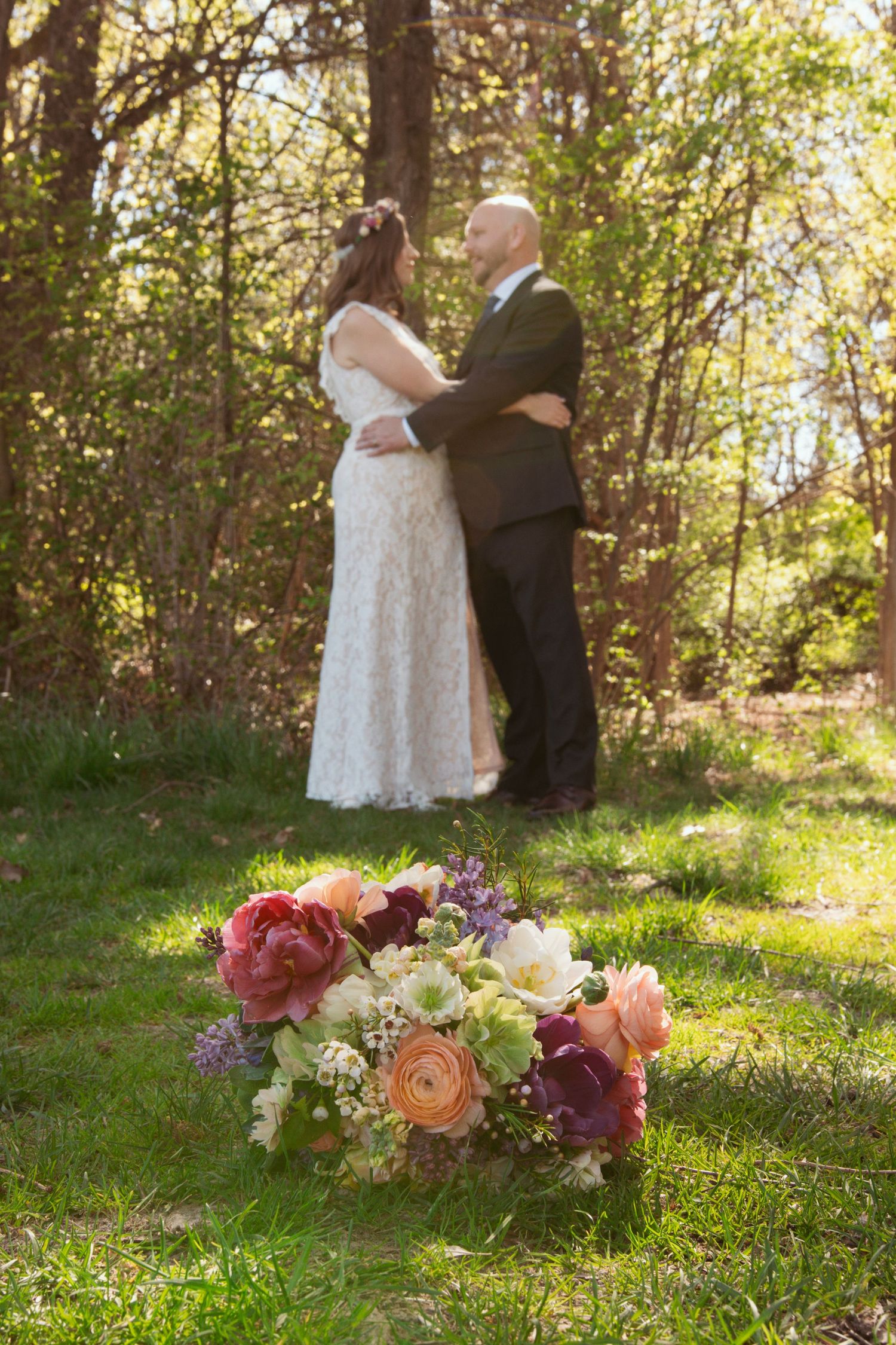 Wedding couple in a sunlit forest with flower bouquet in foreground.