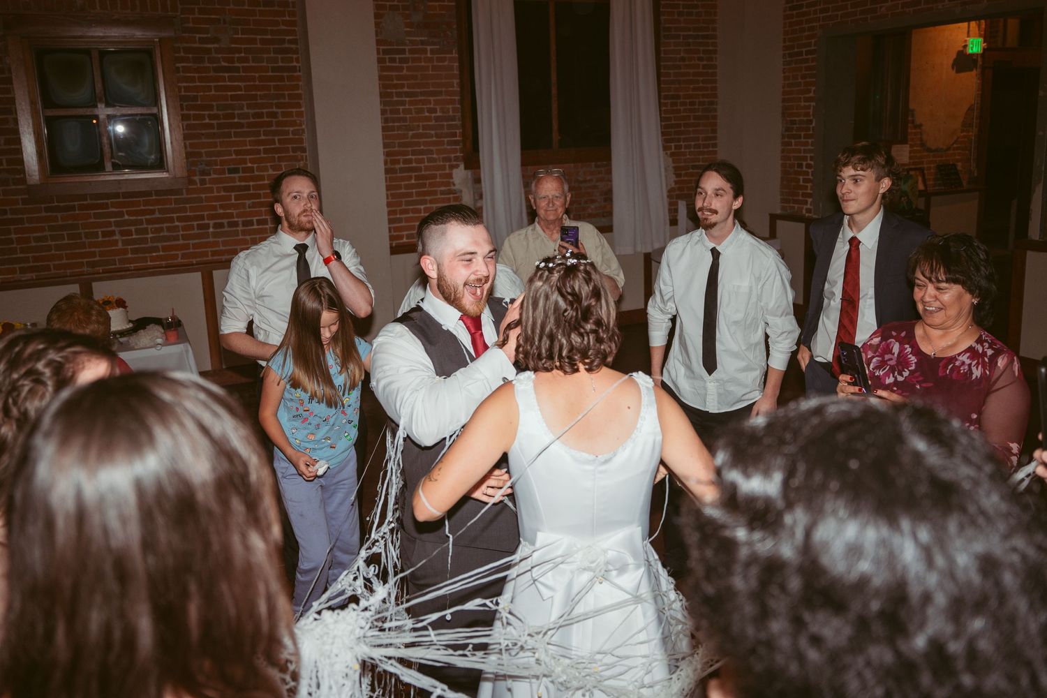 Wedding celebration in brick venue with guests throwing streamers around couple in white dress.