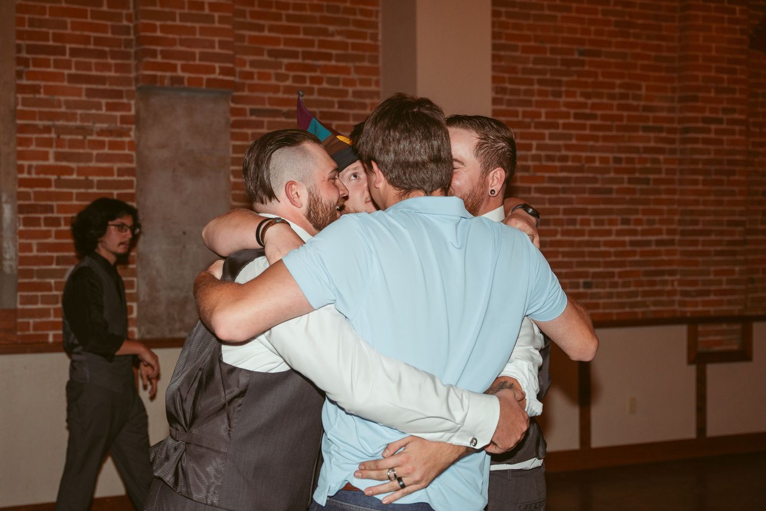 Group of people sharing an emotional embrace in a brick-walled venue during a celebration.