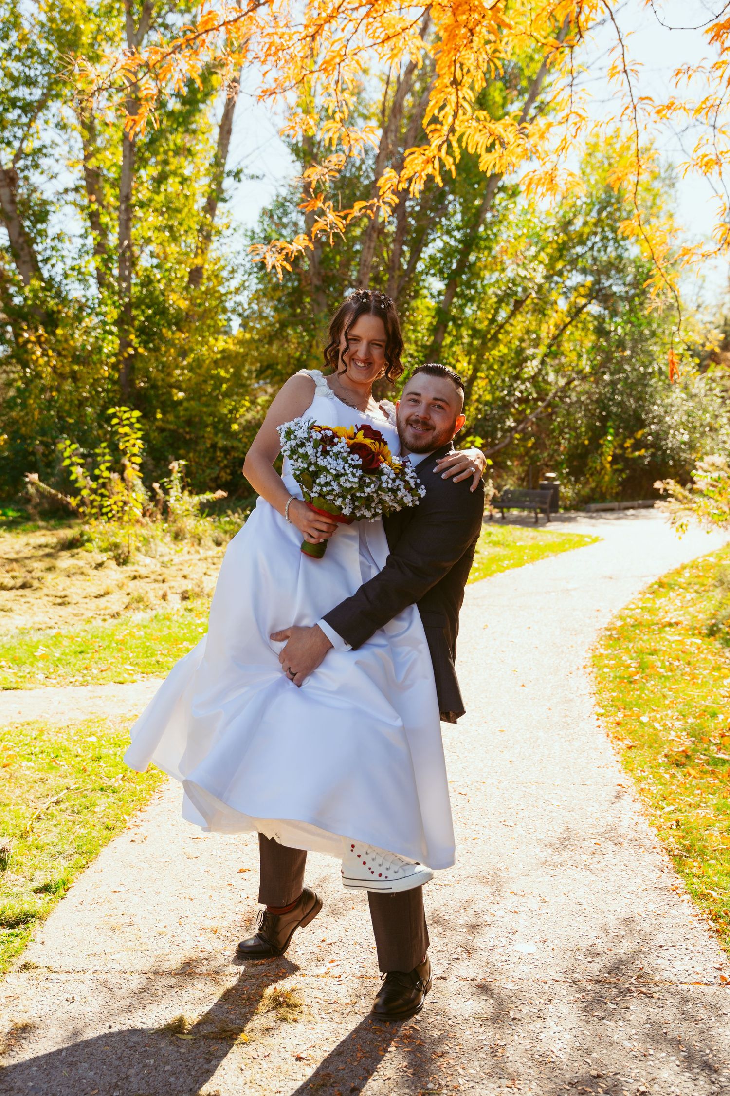 A couple shares a romantic moment on a sunlit path surrounded by fall colors.