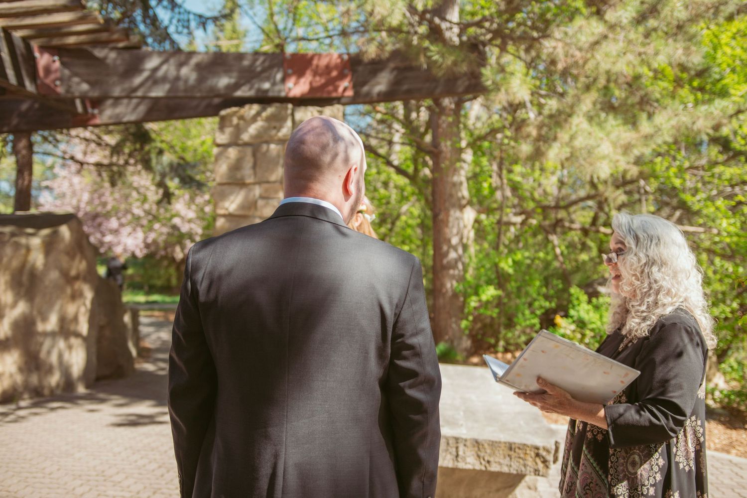 A couple dances together on a stone patio surrounded by lush greenery and trees.