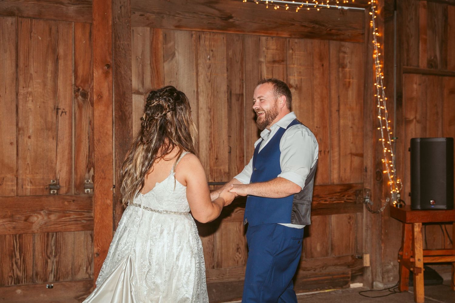 Couples dance together in a rustic barn venue decorated with string lights.