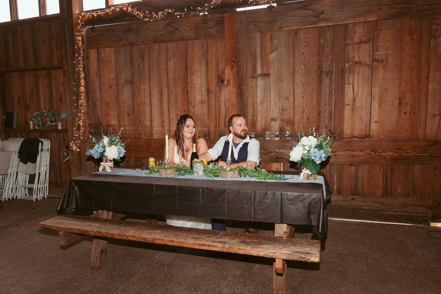 Interior view of a rustic barn wedding reception with wooden walls and string lights.