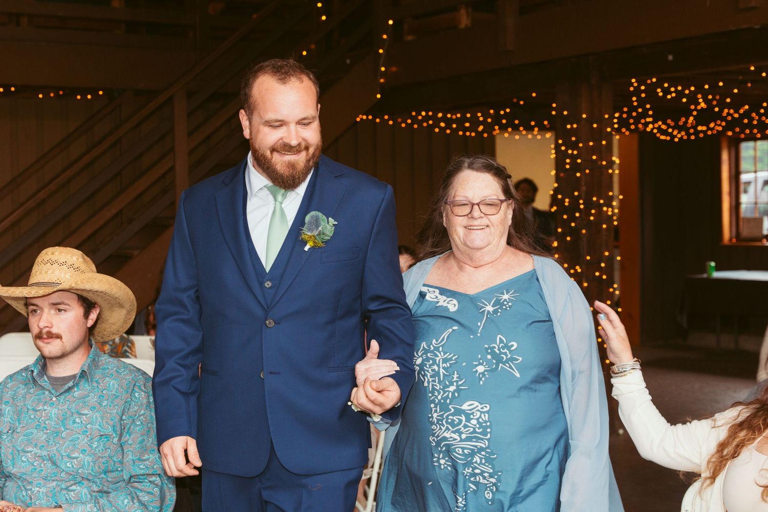 Wedding party dancing and celebrating in a rustic barn venue decorated with string lights.