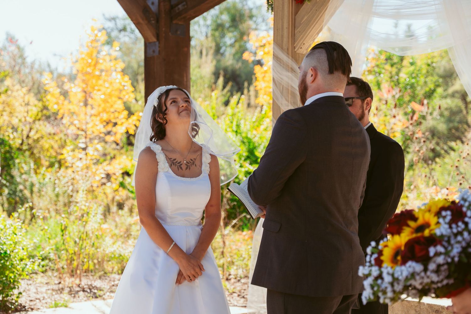 Sunlit wedding ceremony captures intimate exchanges between couple under rustic pavilion.