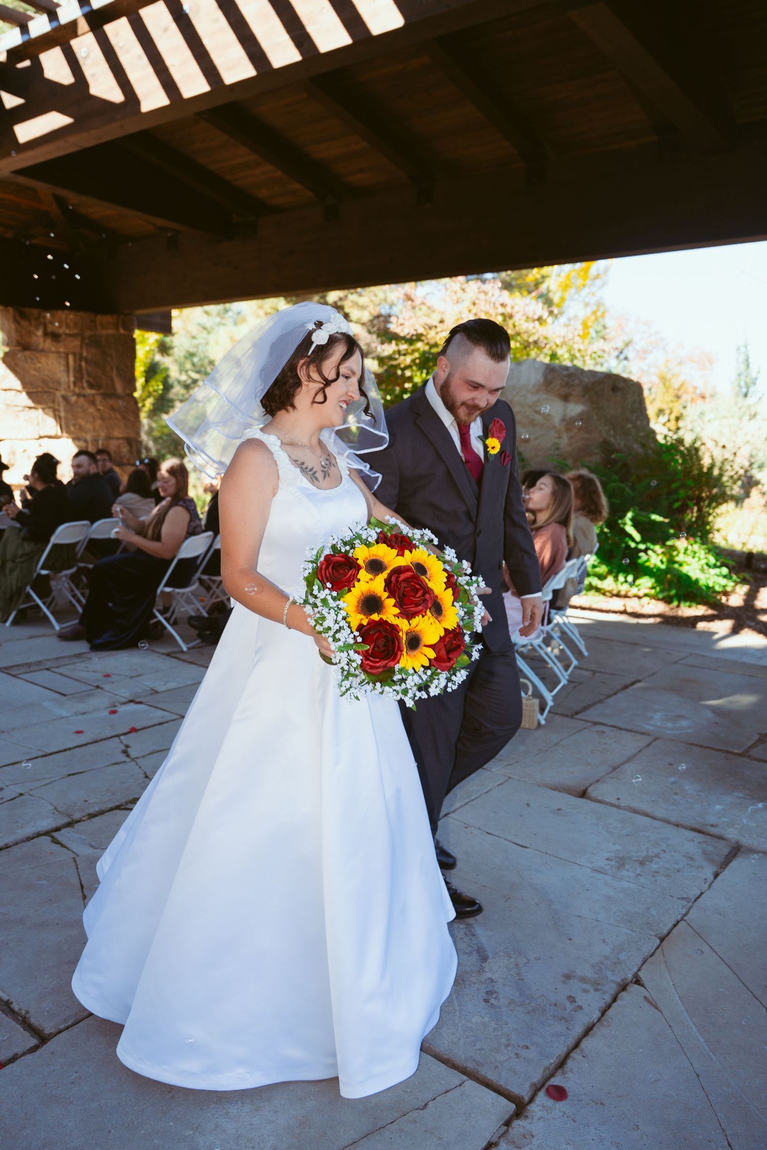 Wedding couple dancing under a rustic wooden pavilion with sunflowers in the bride's bouquet.