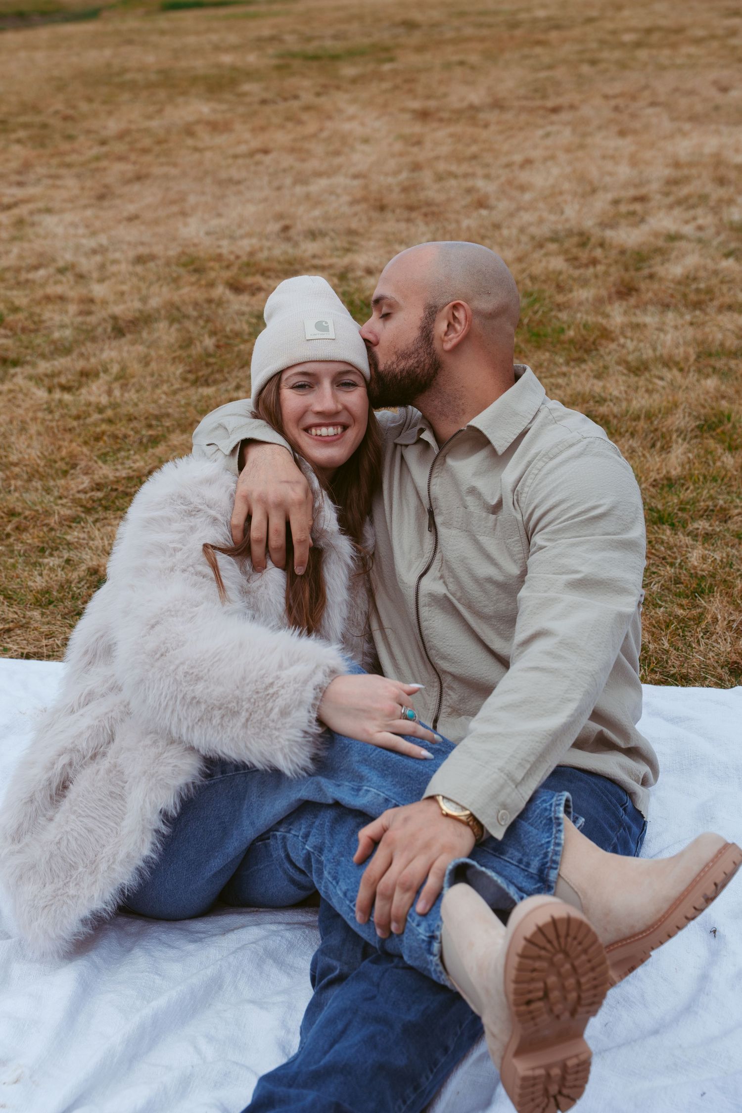 Couple laughing together while relaxing on white blanket outdoors.