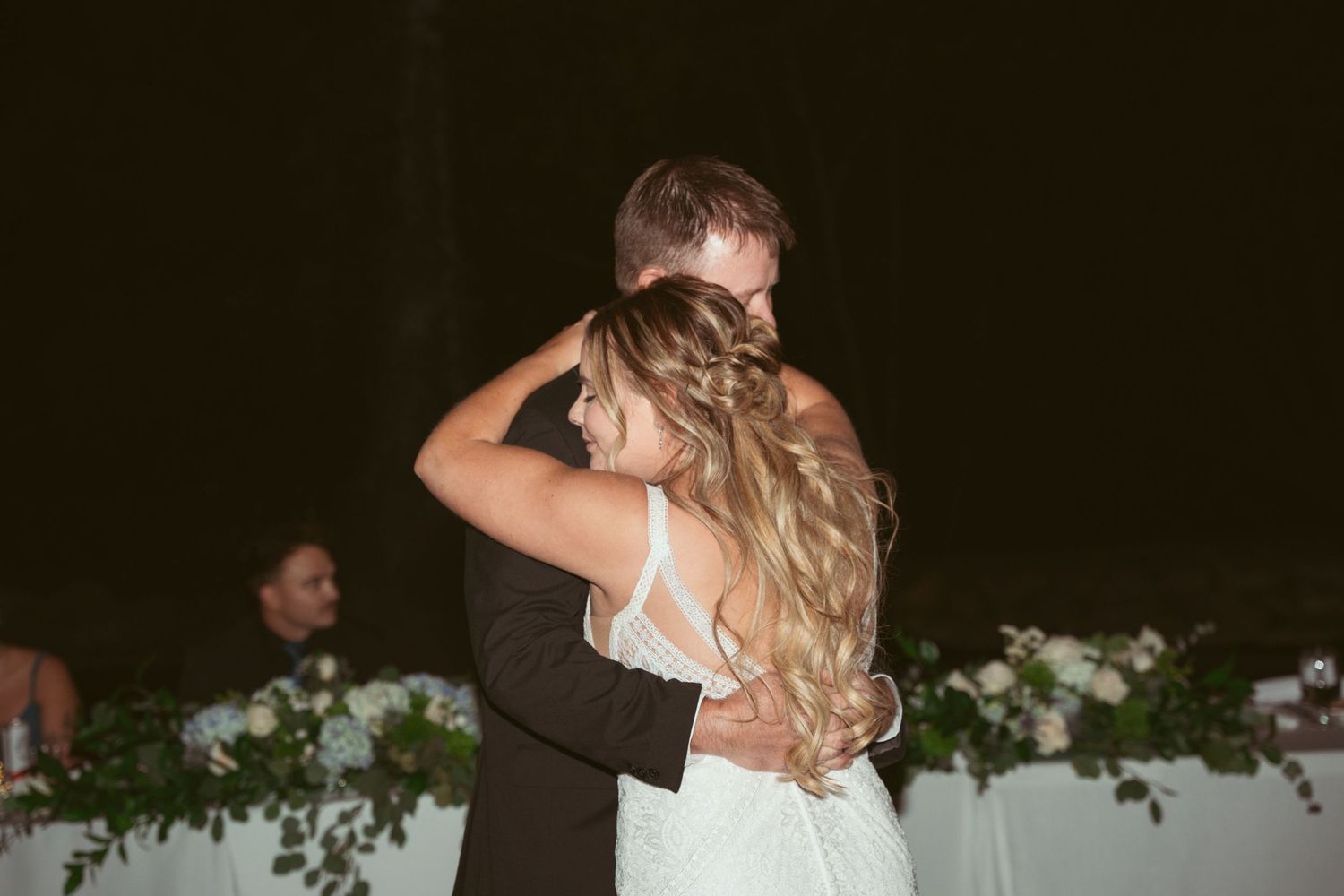 Couple sharing their first dance at outdoor wedding reception with decorative lighting.