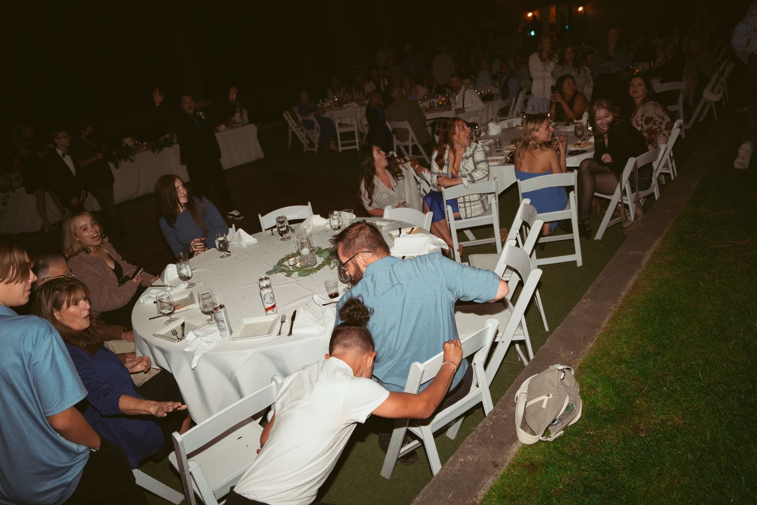 Wedding reception dining area with white chairs and tables set up under twinkling lights at night.