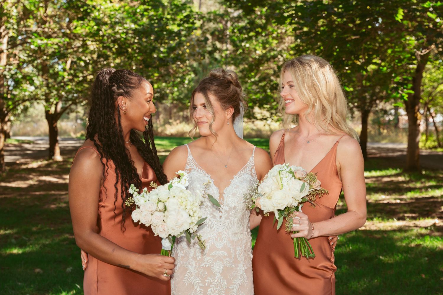 Bridal party in orange dresses and white gown celebrate outdoors.