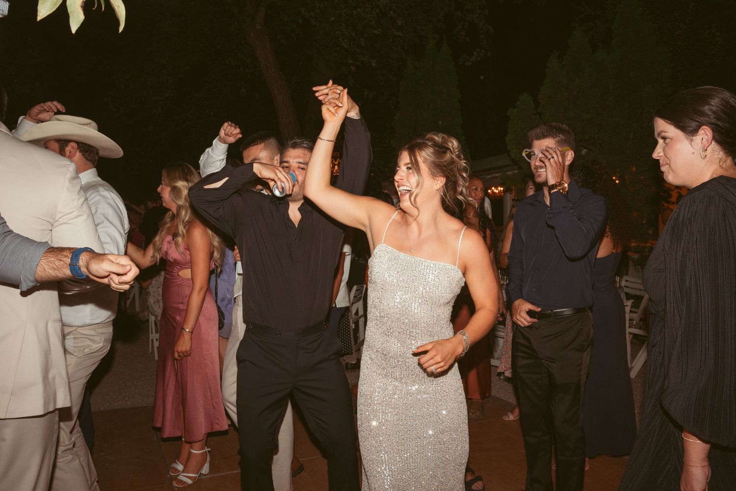 Wedding guests dancing and celebrating on a dimly lit outdoor dance floor.