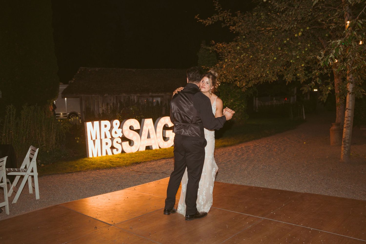 Nighttime wedding celebration with illuminated MRS sign and guests dancing.