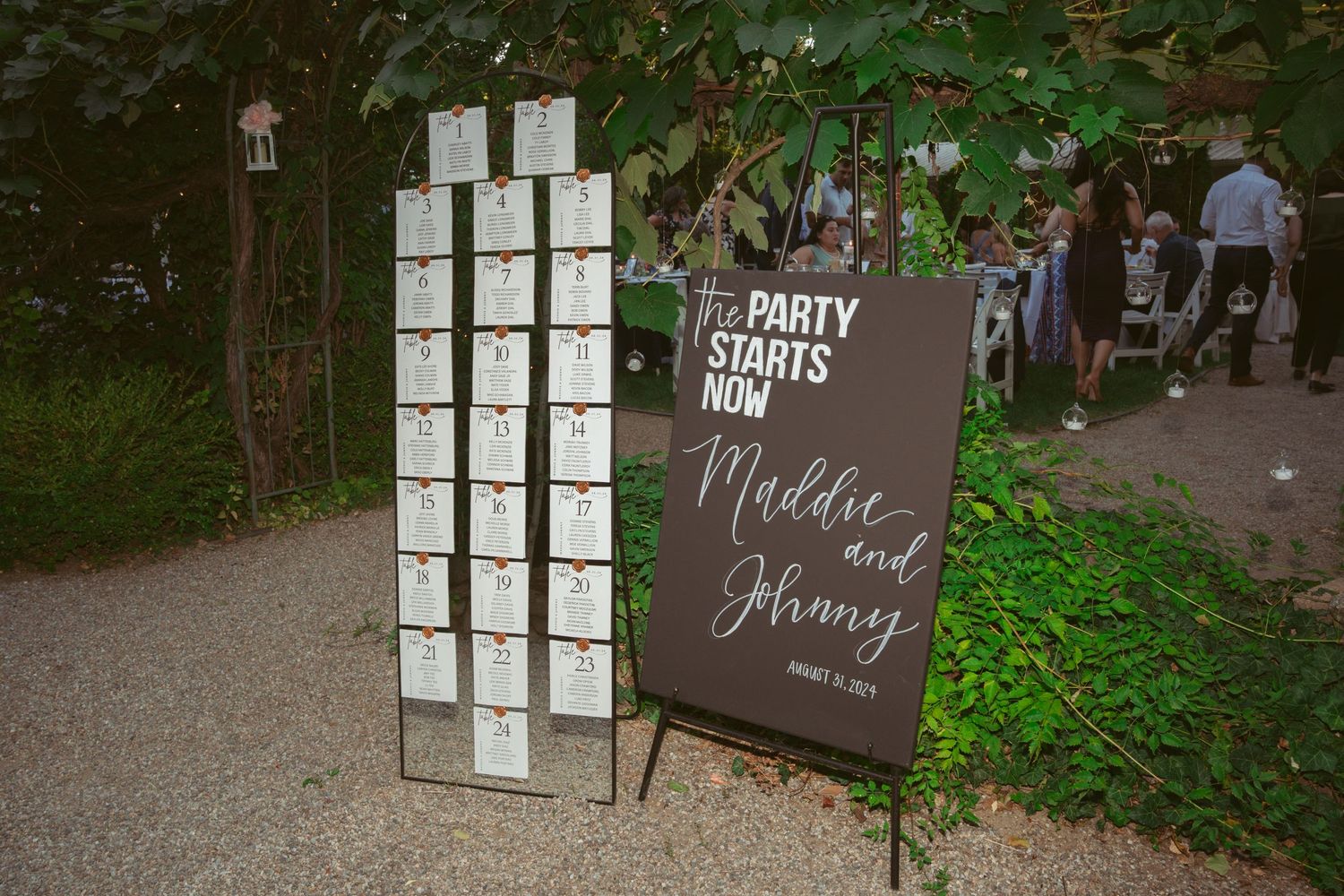 Wedding seating chart display with photo frames arranged on dark board in outdoor garden setting.