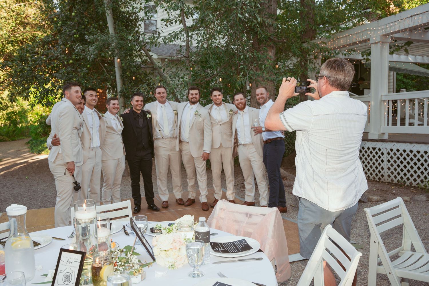 Wedding party members in light colored attire gather for group photos on an outdoor deck.