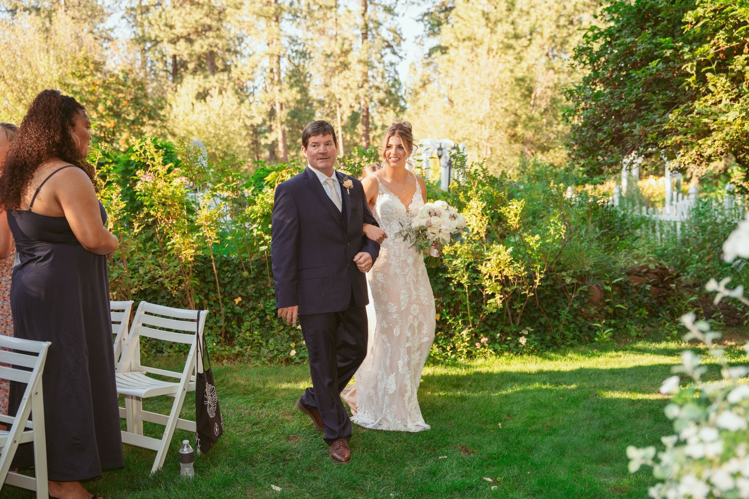 Wedding ceremony processional on manicured lawn with garden backdrop.
