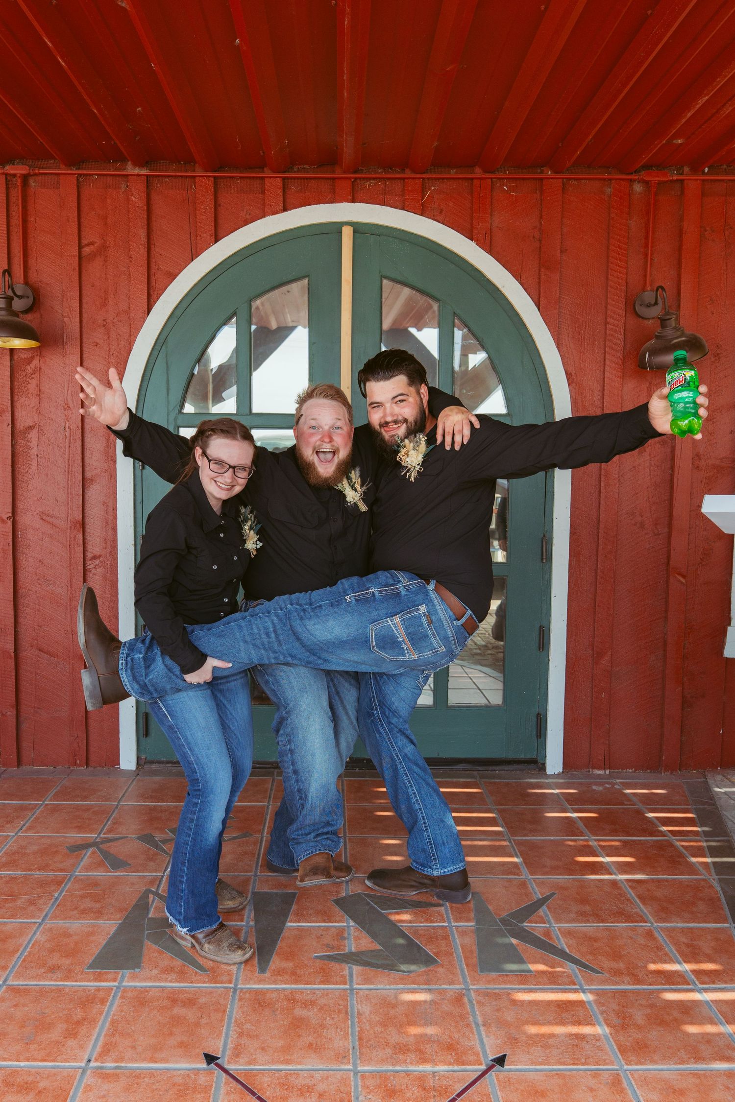 Three people pose playfully in front of a red building with a teal arched doorway.