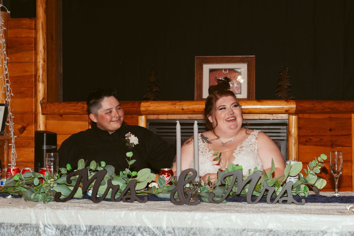 People seated at a rustic wooden table decorated with greenery during an outdoor event.