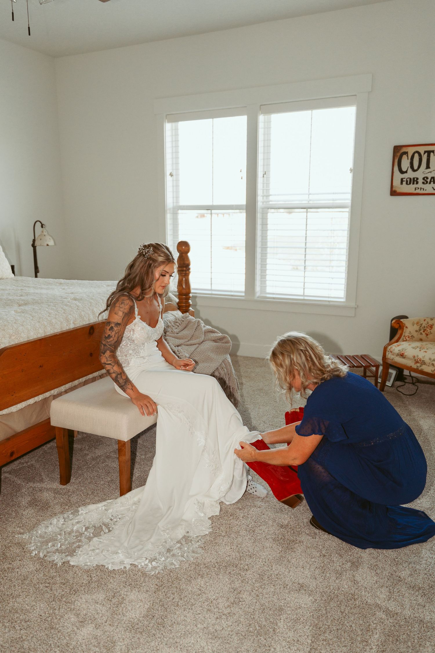 Two people on carpet floor, one in a white dress and another in navy blue, during wedding preparations.