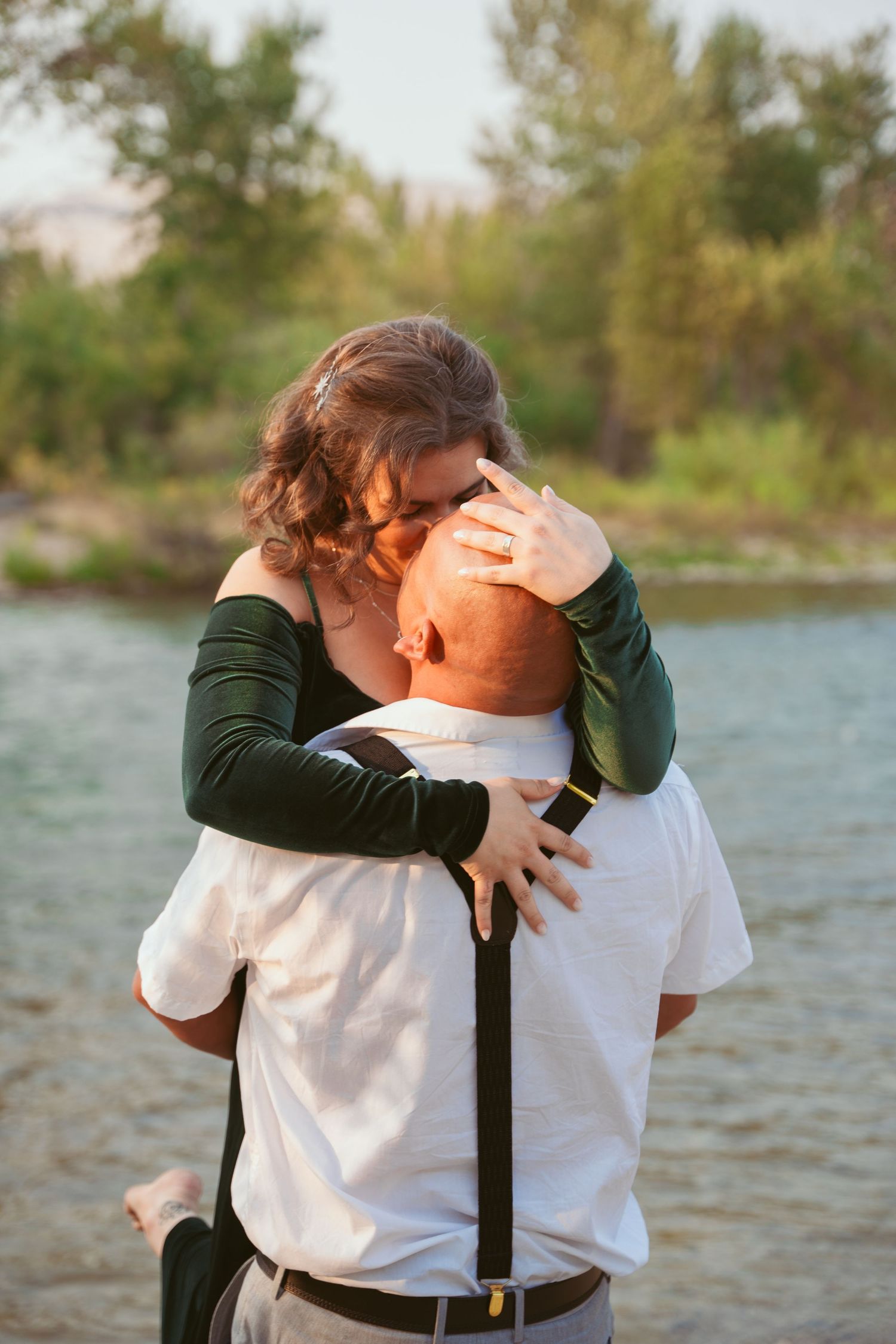 Two people embrace emotionally during an outdoor photoshoot by a lake.