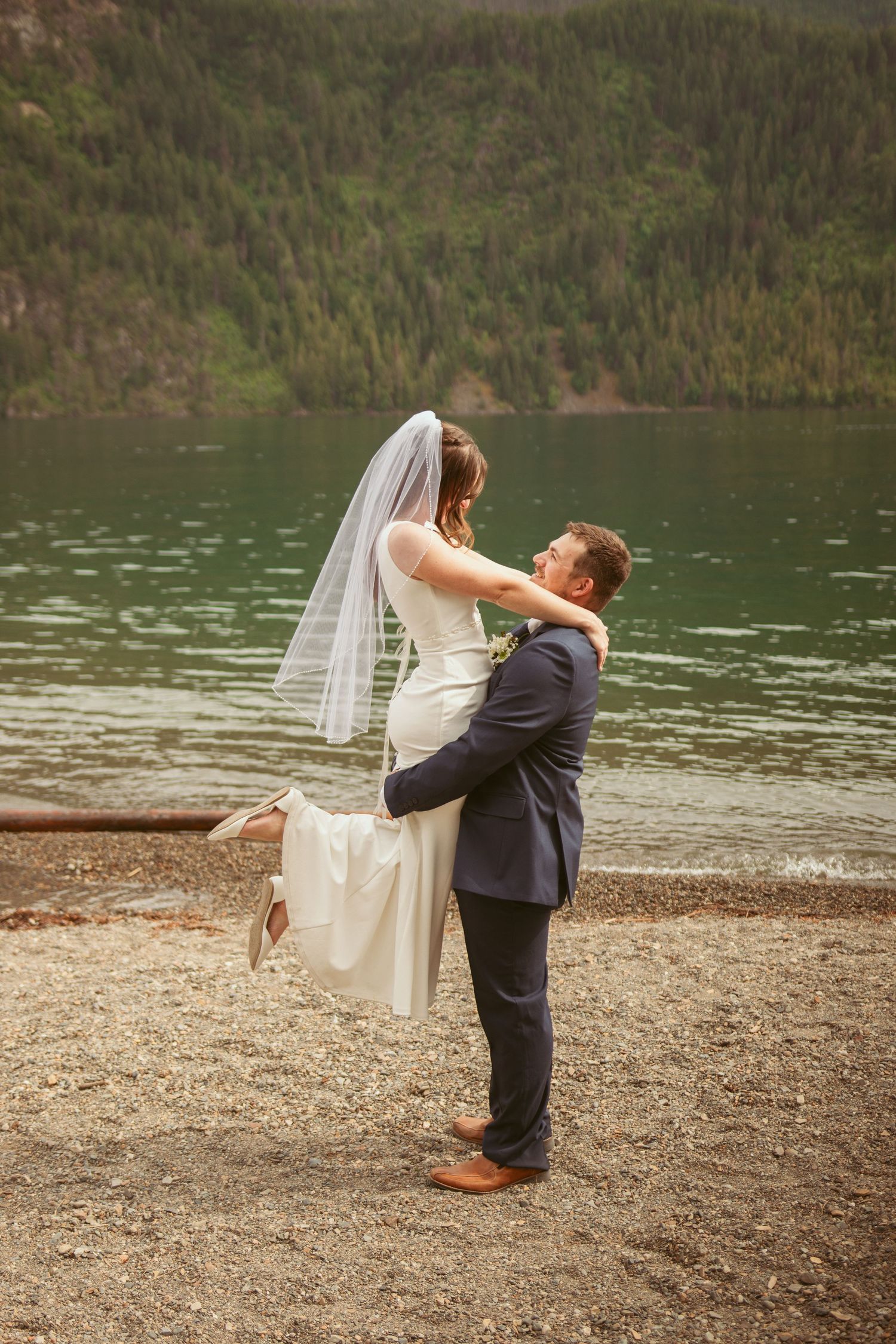 Romantic lakeside wedding photos with mountain and forest backdrop.