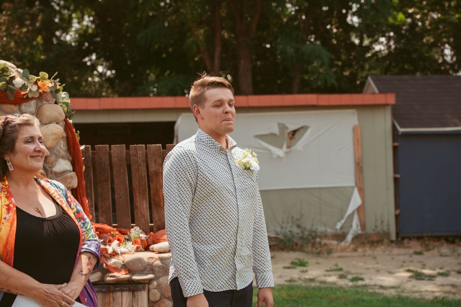 Wedding party members gathered outdoors near a wooden fence during ceremony proceedings.