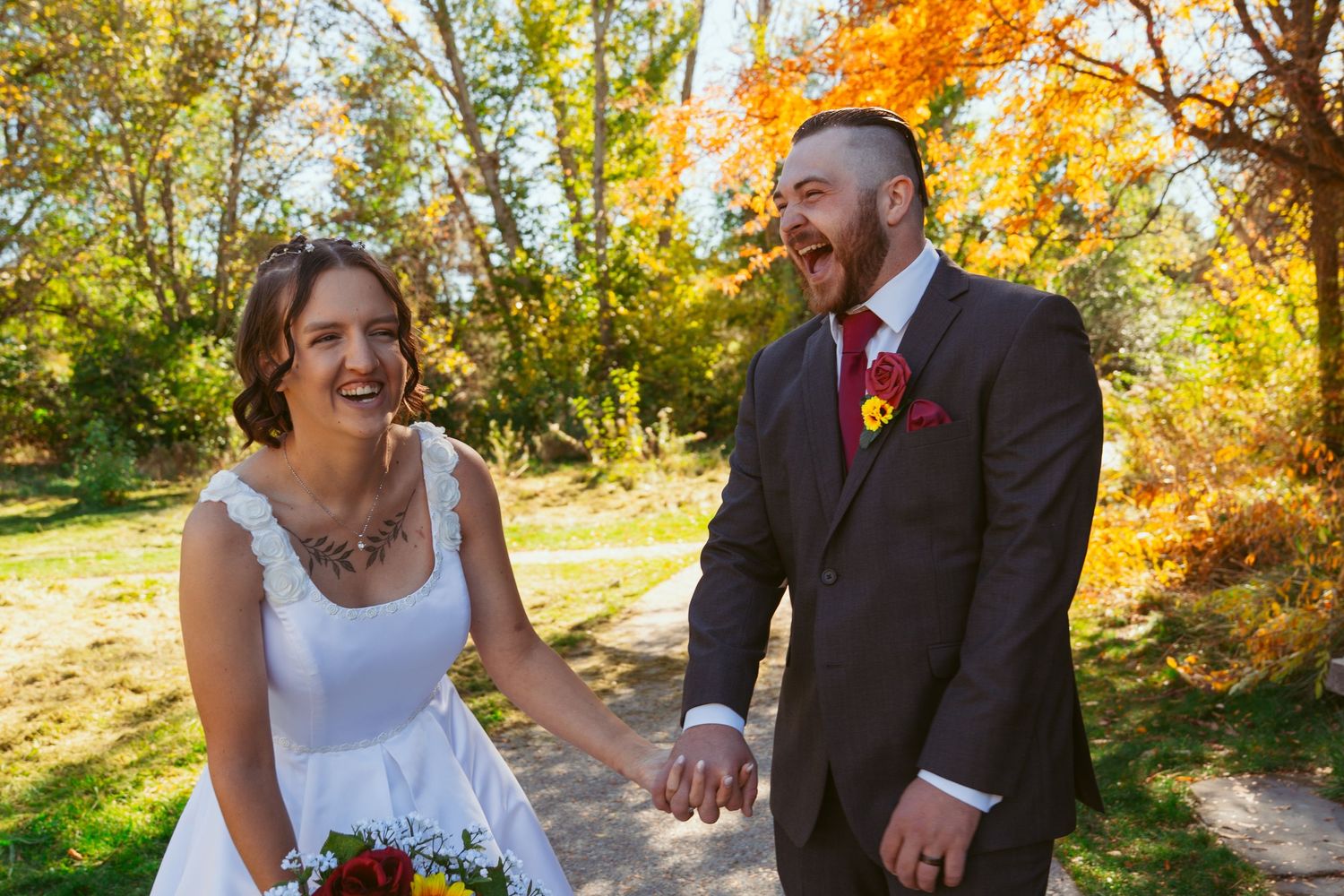 A couple shares a joyful moment on a scenic fall trail with golden trees in the background.