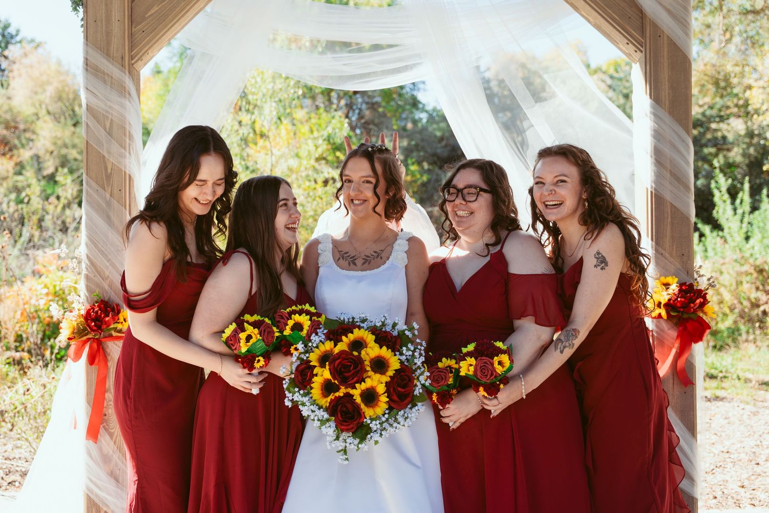 Wedding group shares candid moment under wooden pavilion with white draping.
