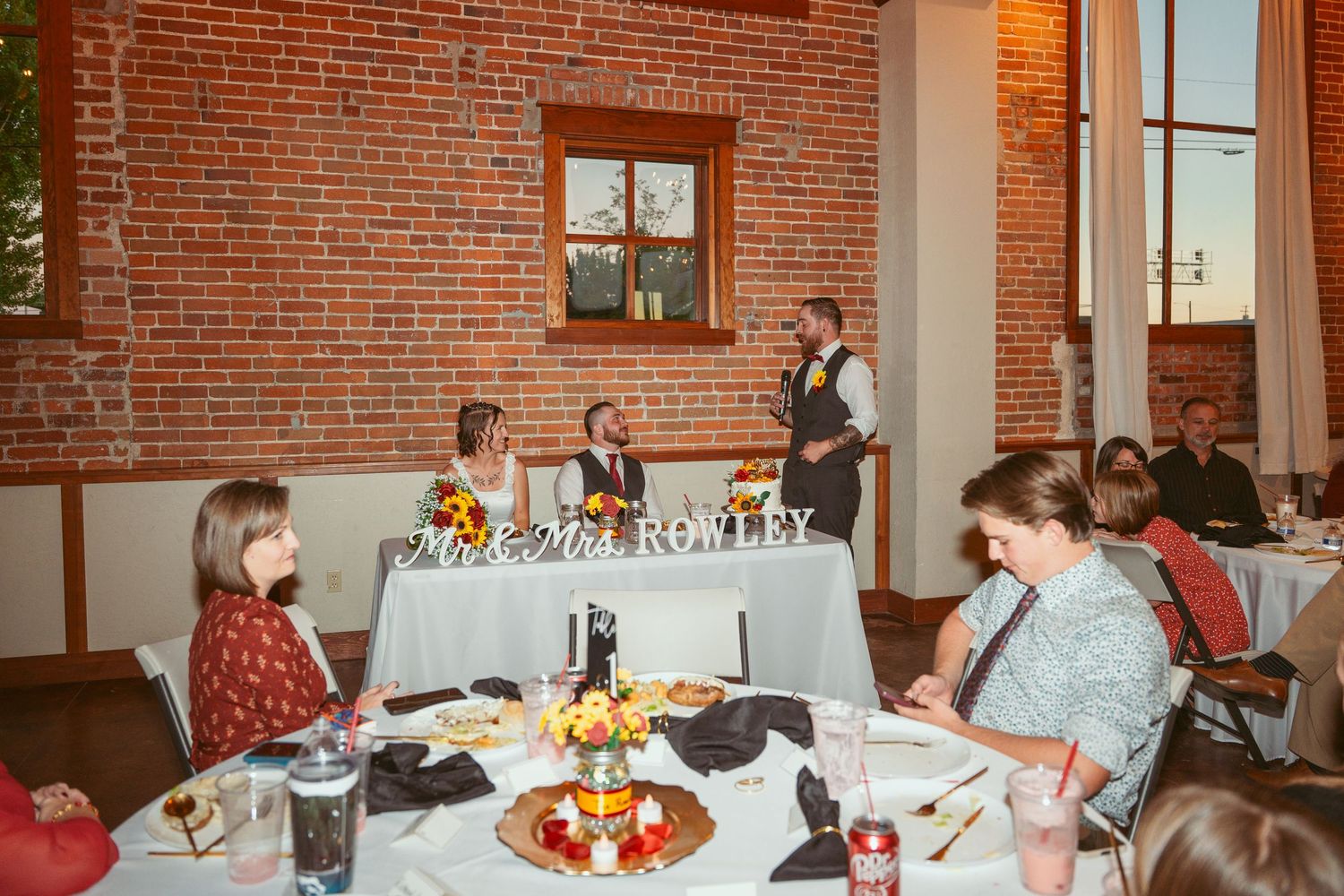 Reception venue features exposed brick walls and elegant table settings with floral centerpieces.
