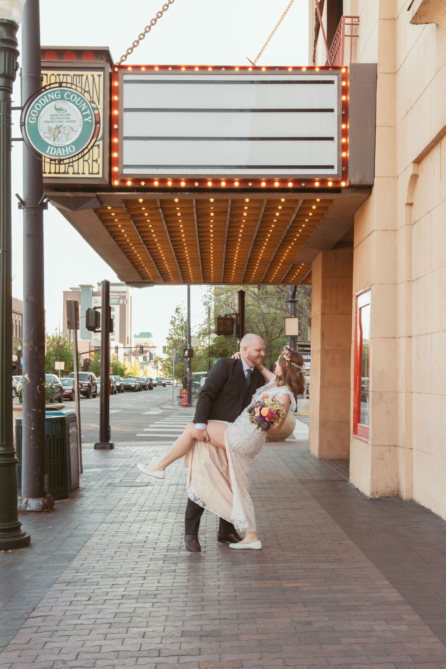 Playful wedding couple performs dramatic dip pose under vintage theater marquee.
