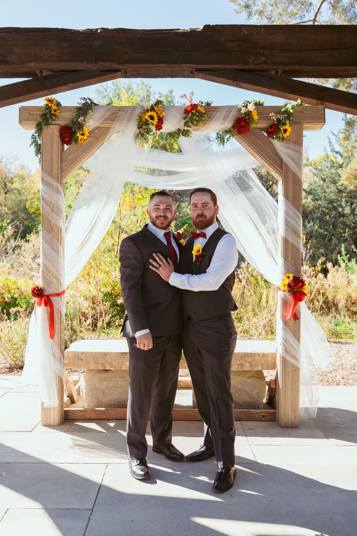 Groomsmen share laughs and poses under decorated wedding pavilion with white draping.