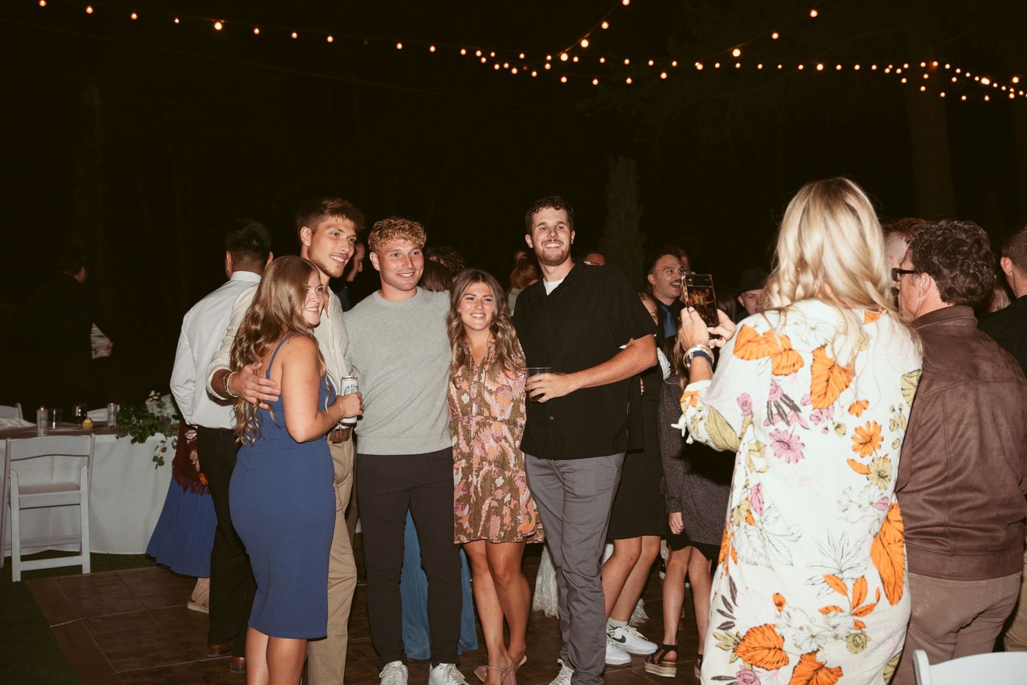 Group of guests socializing at an outdoor evening party under string lights.