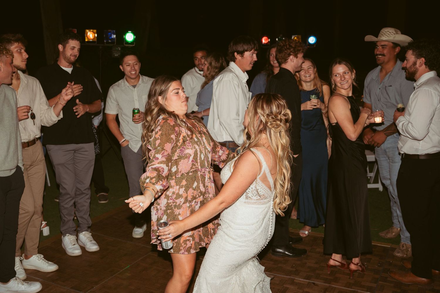 Wedding guests dance and celebrate on a crowded dance floor at an indoor reception venue.