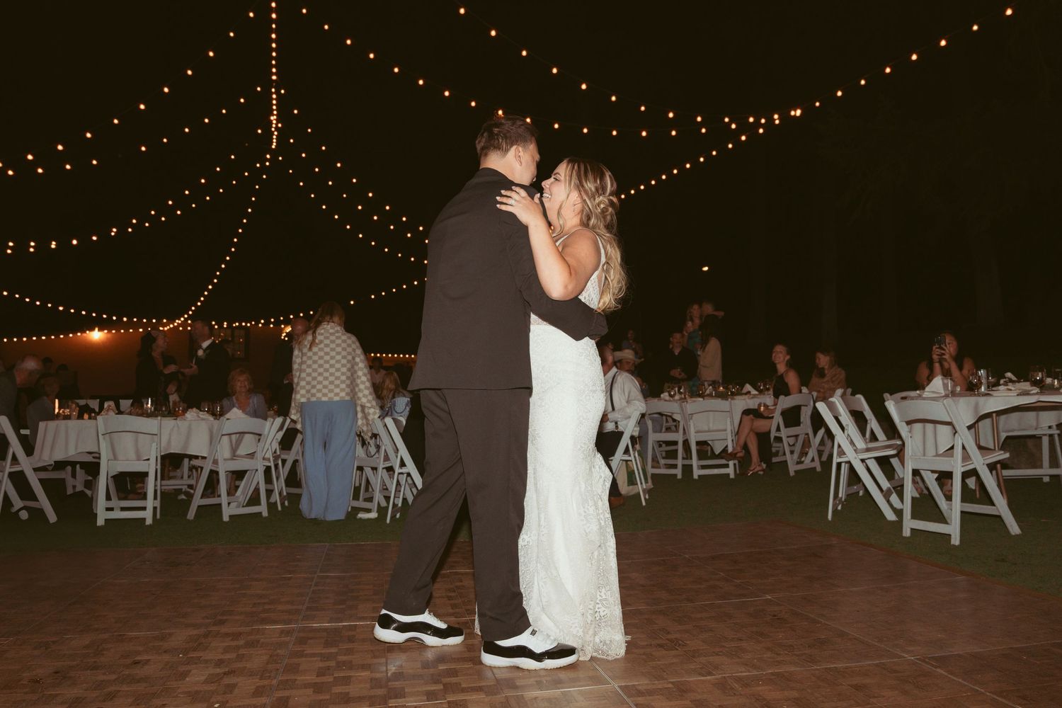 Outdoor wedding reception setup with string lights and white folding chairs.