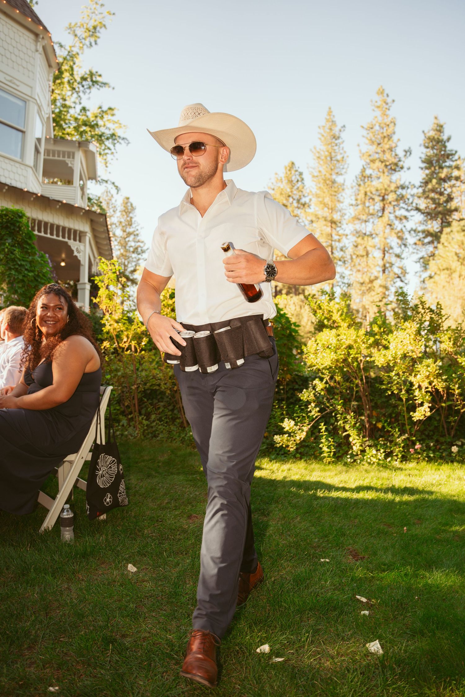 A western-themed outdoor celebration with guests dancing on a grassy lawn at golden hour.