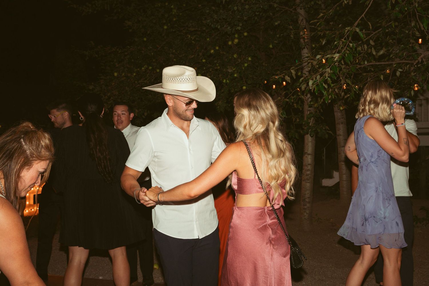 Couples dancing at a nighttime wedding reception with string lights and rustic outdoor decor.