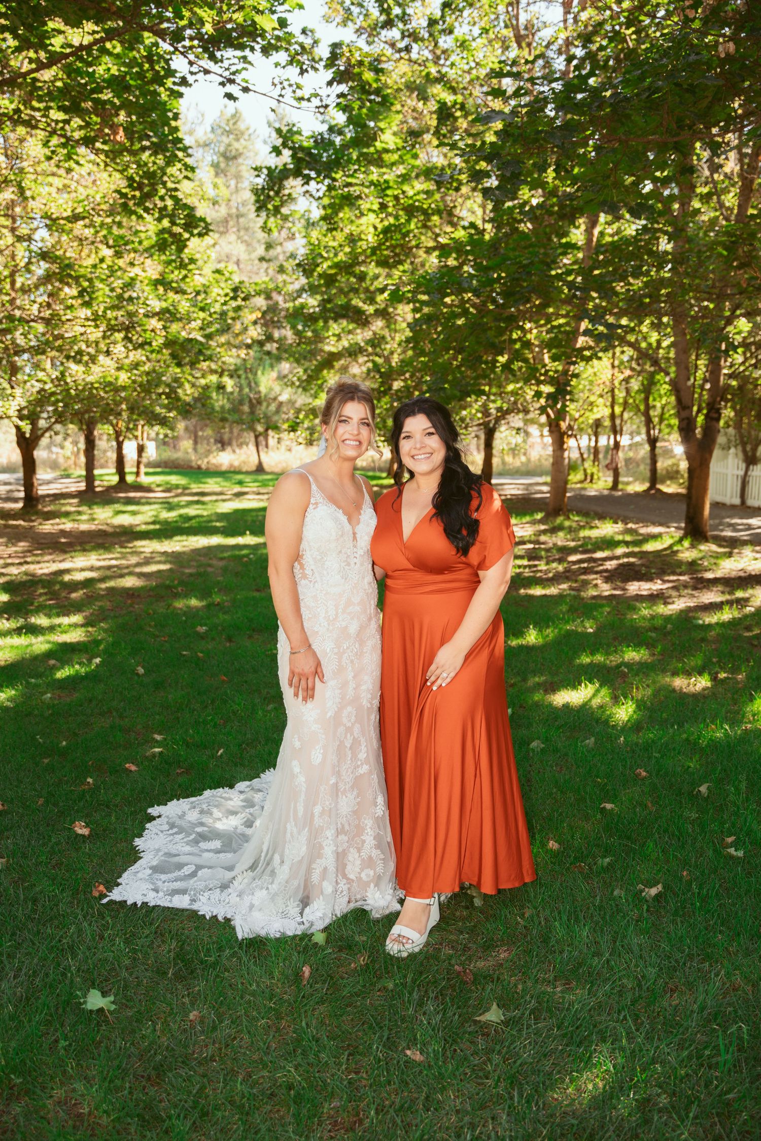 Two people in formal attire standing together on grass in a sunlit garden setting.