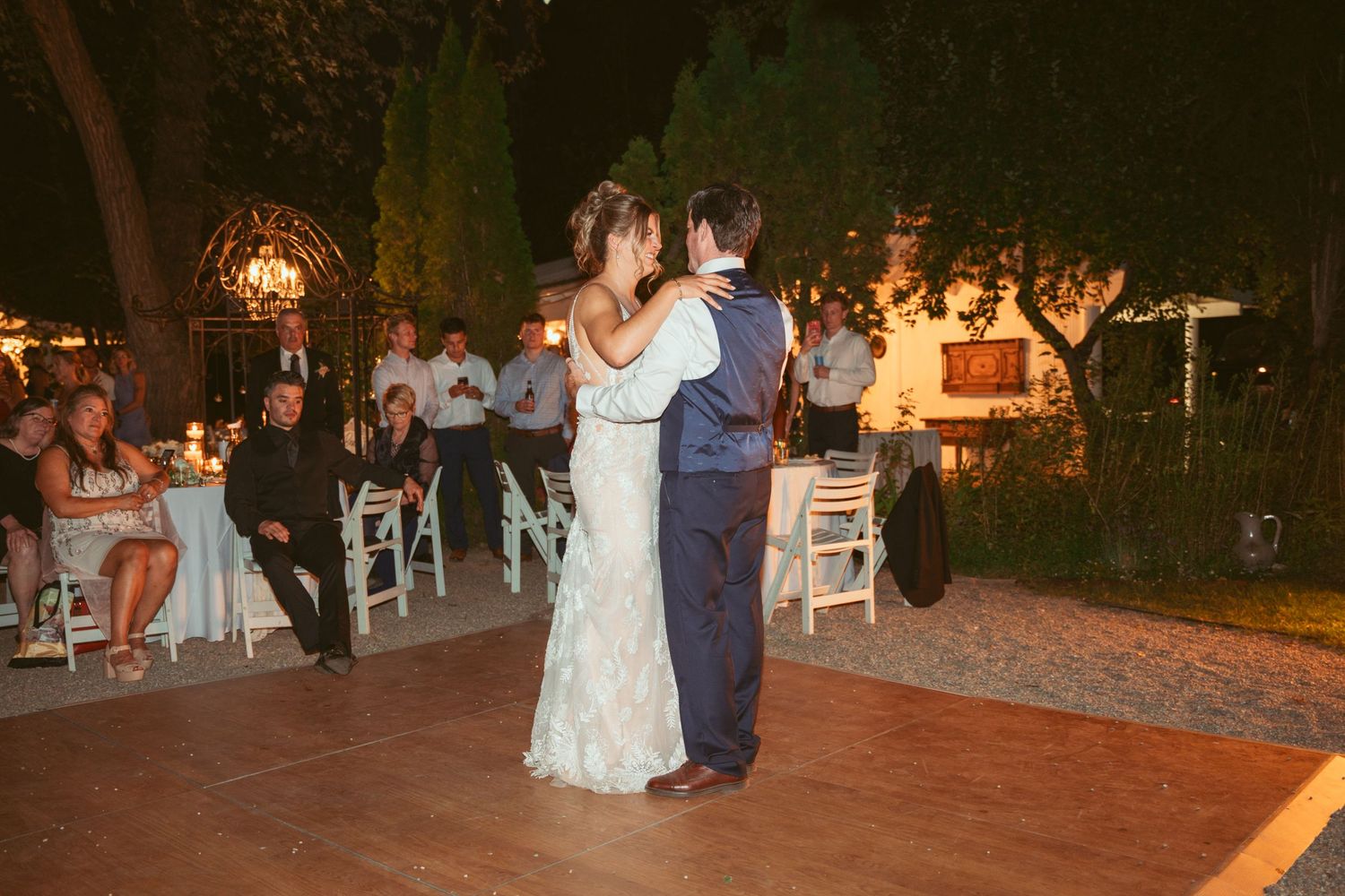 A couple shares an intimate dance moment on a wooden dance floor at their outdoor evening wedding.