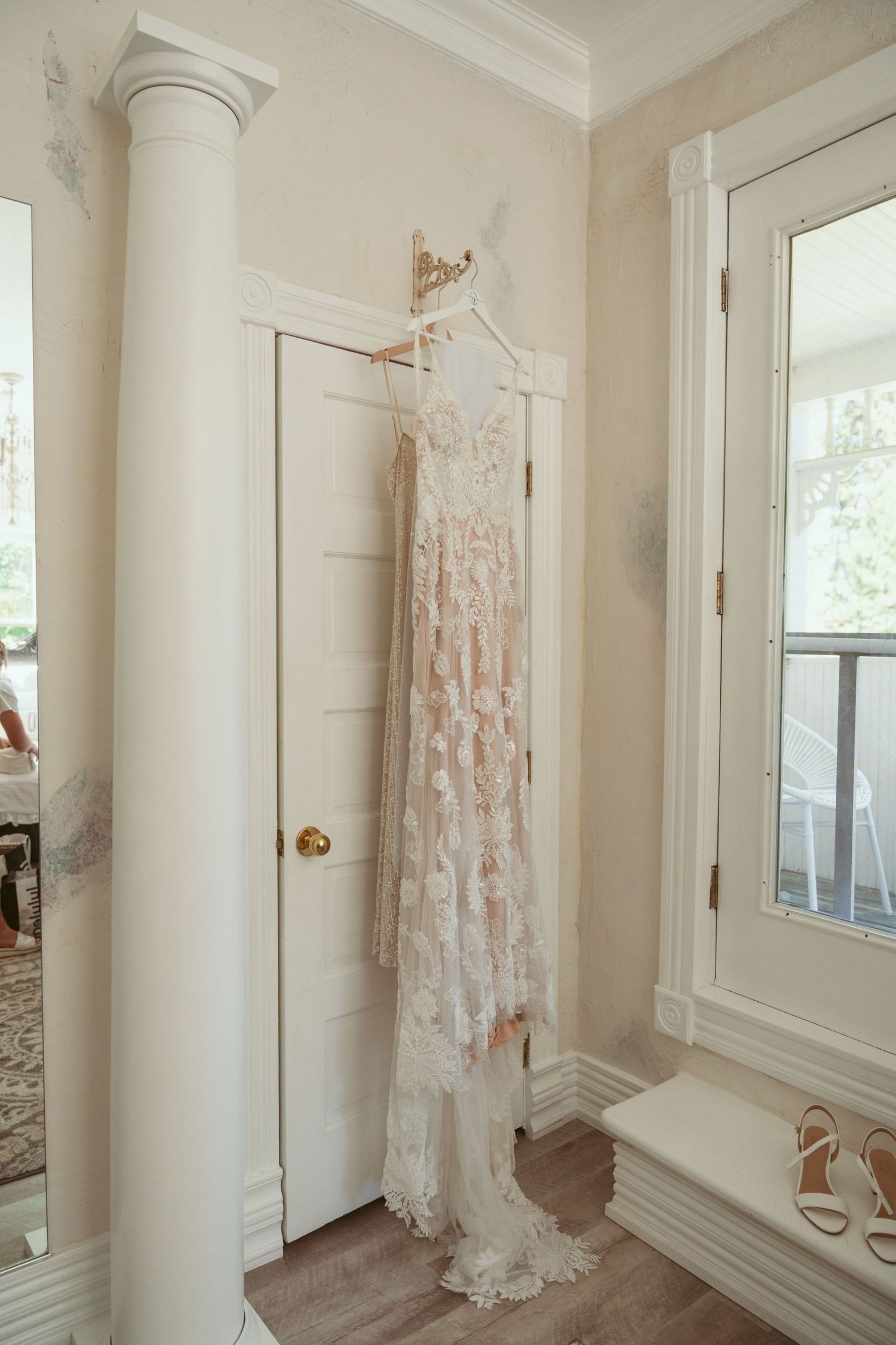 White lace wedding dresses and formal gowns hang elegantly in a bright, sunlit dressing room with white walls.