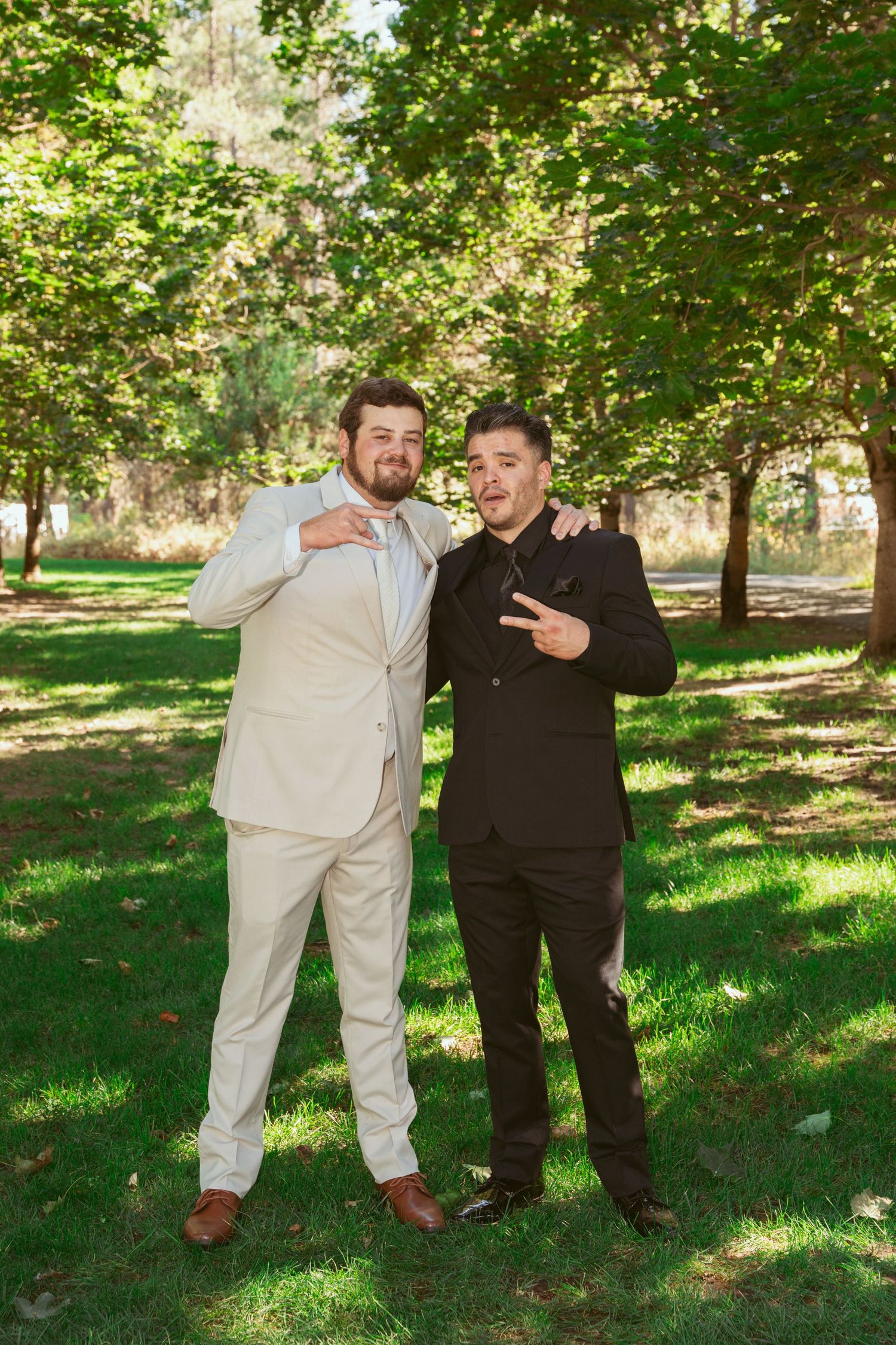 Two people in contrasting black and white outfits pose playfully together in a sunny park setting with green trees.