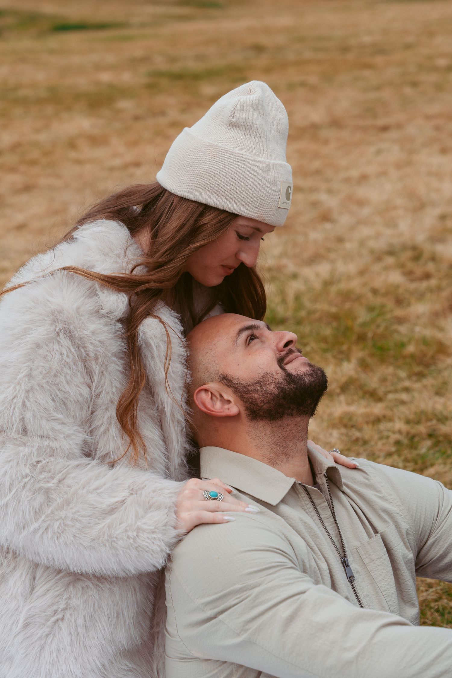 Intimate moment between couple wearing white and beige outfits against a natural outdoor backdrop.