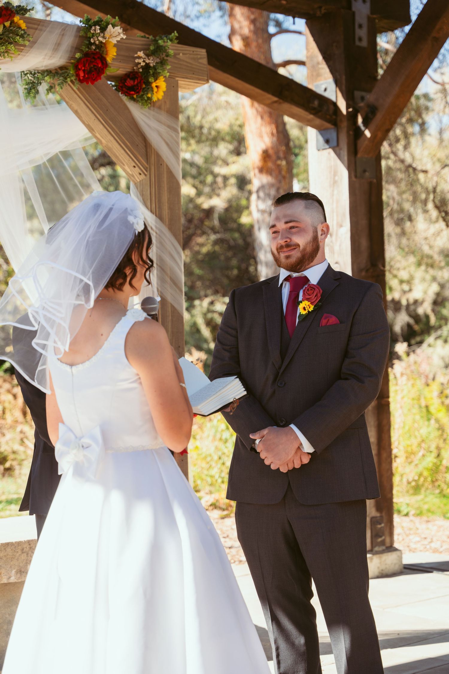 Joyful wedding ceremony exchange beneath wooden pergola decorated with fall flowers.