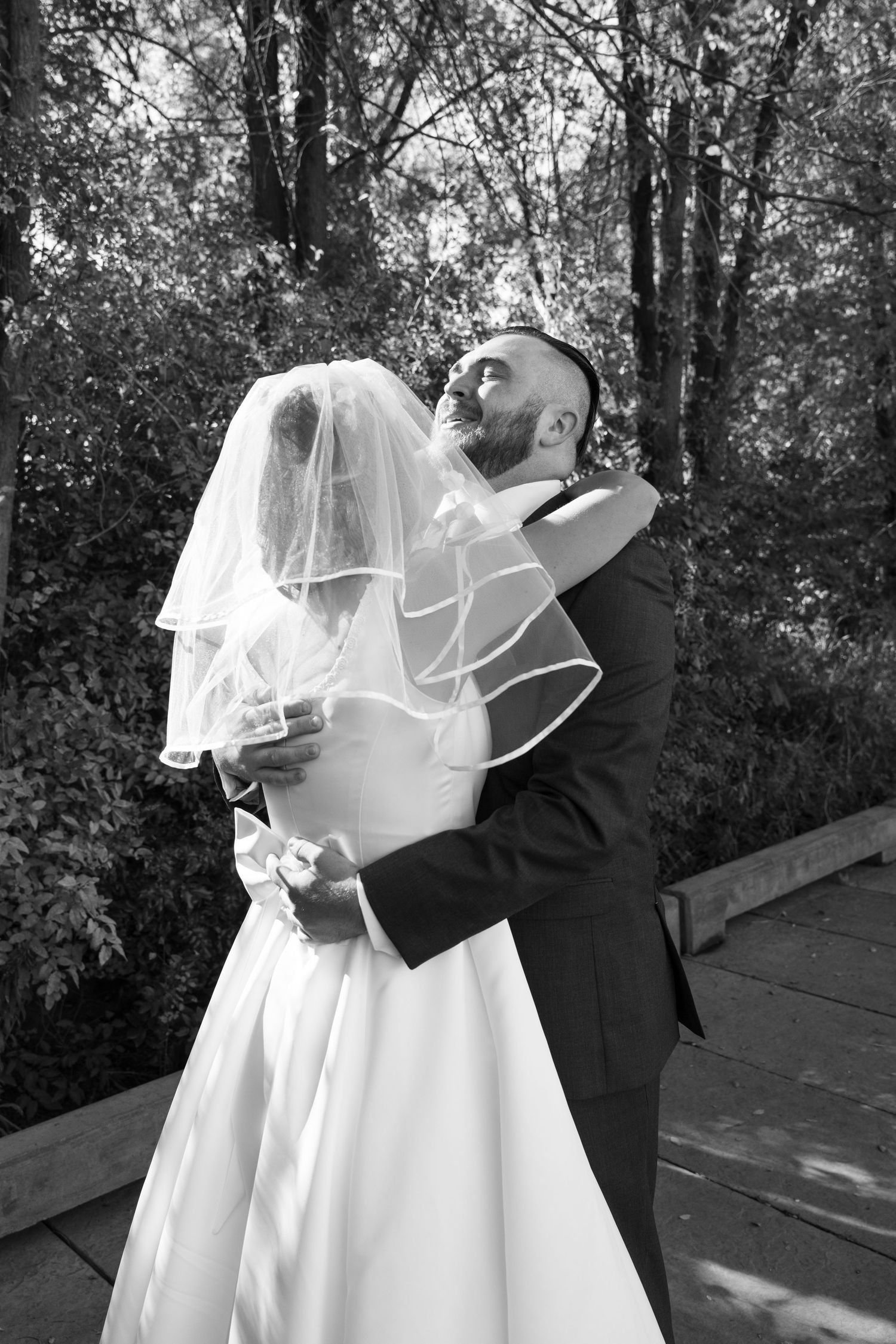 A black and white photo captures an intimate wedding embrace on a wooden deck.