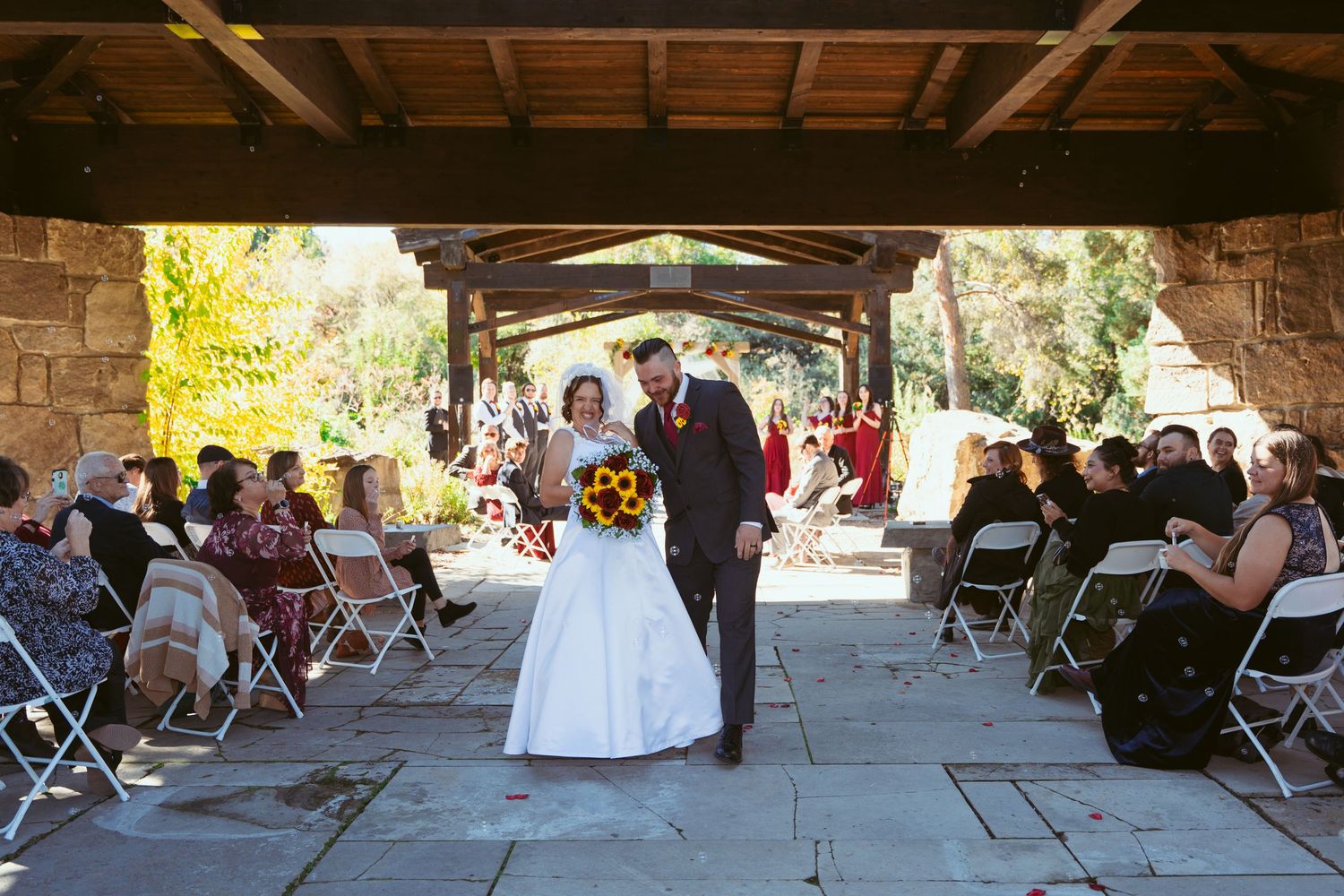 Panoramic view of a wedding venue with wooden roof and stone pillars during an outdoor ceremony.