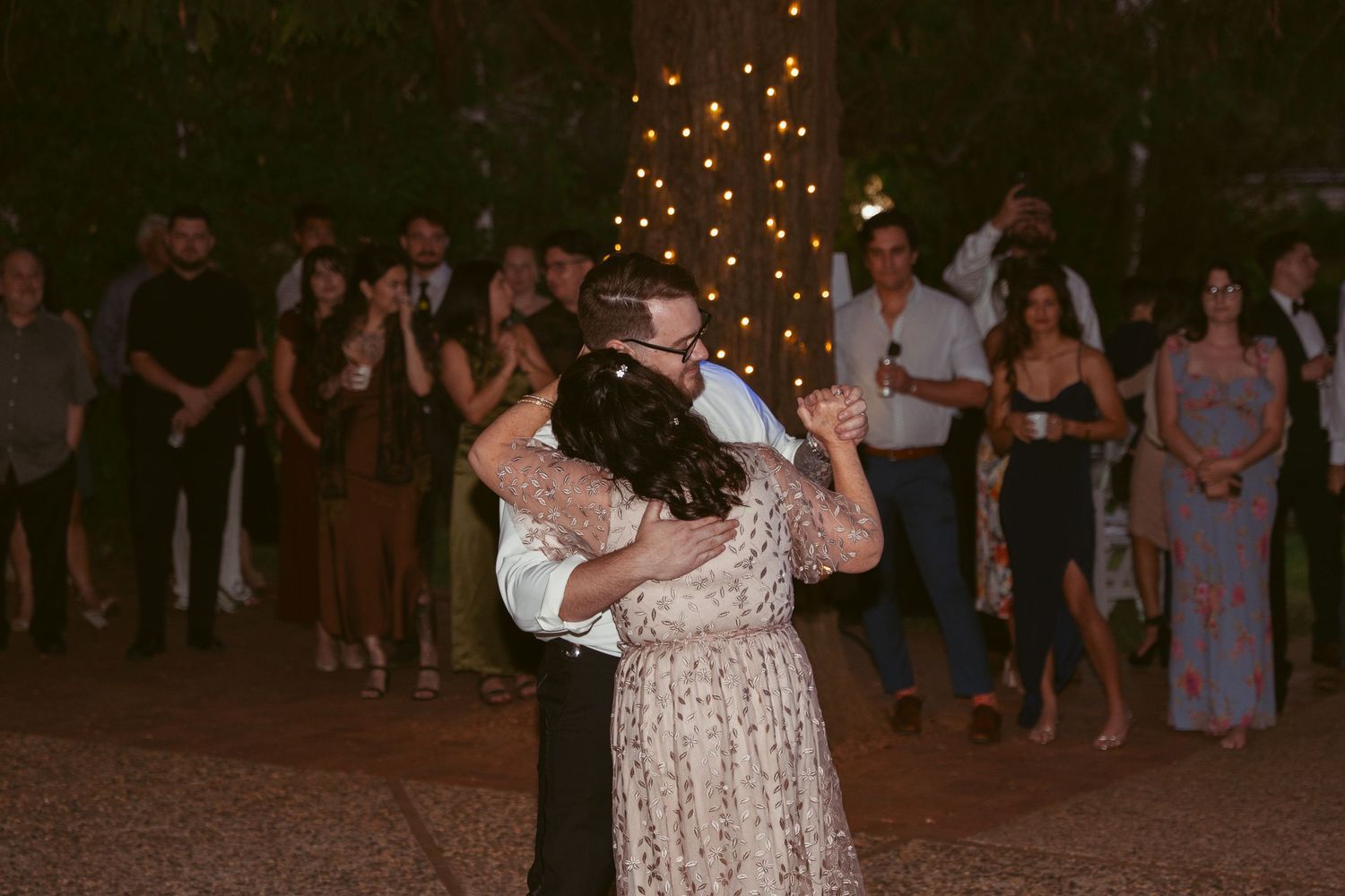 Couples dancing at a rustic outdoor wedding reception under warm string lighting.