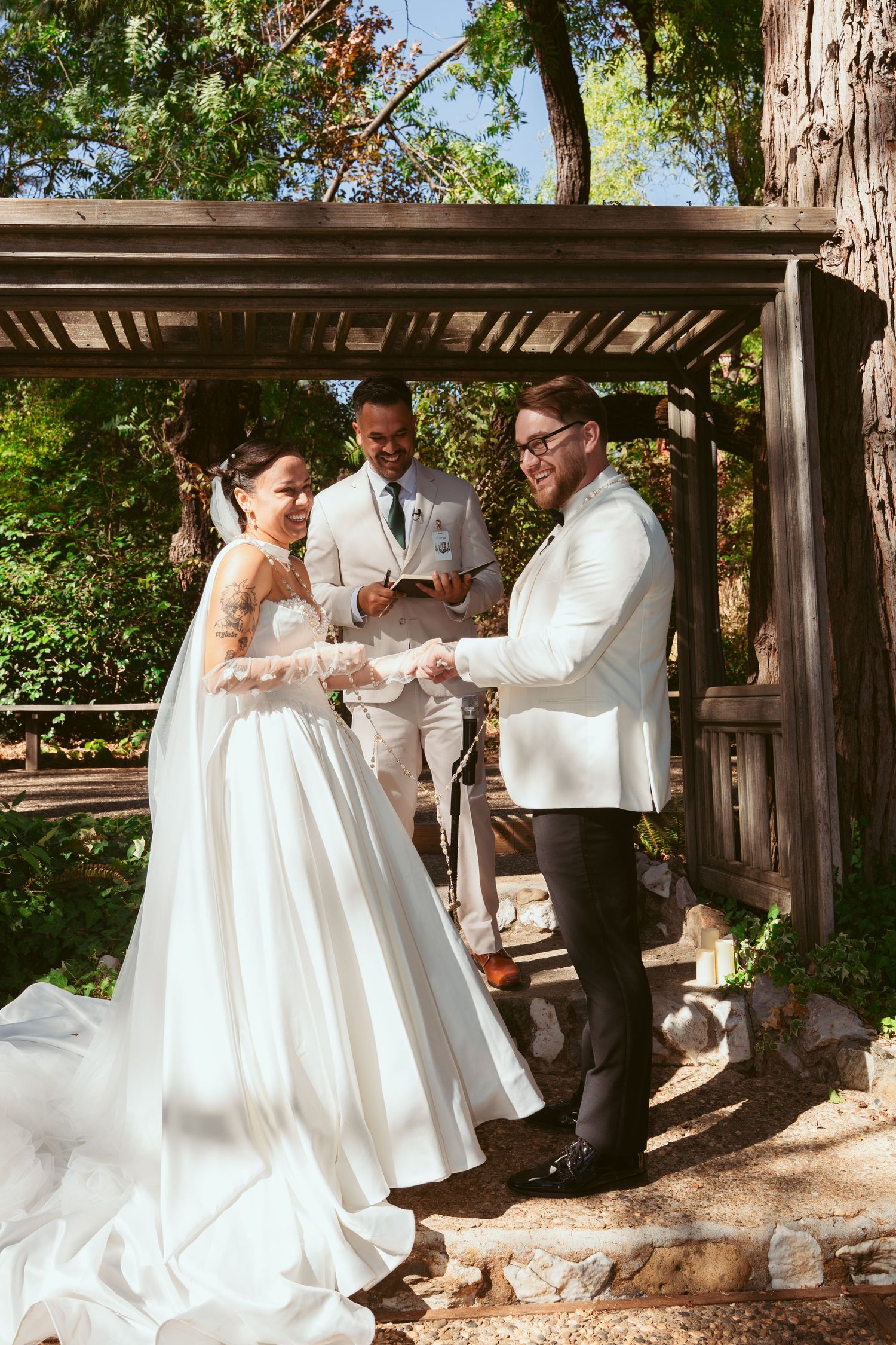Wedding celebration sequence captured under wooden pergola with lush greenery background.