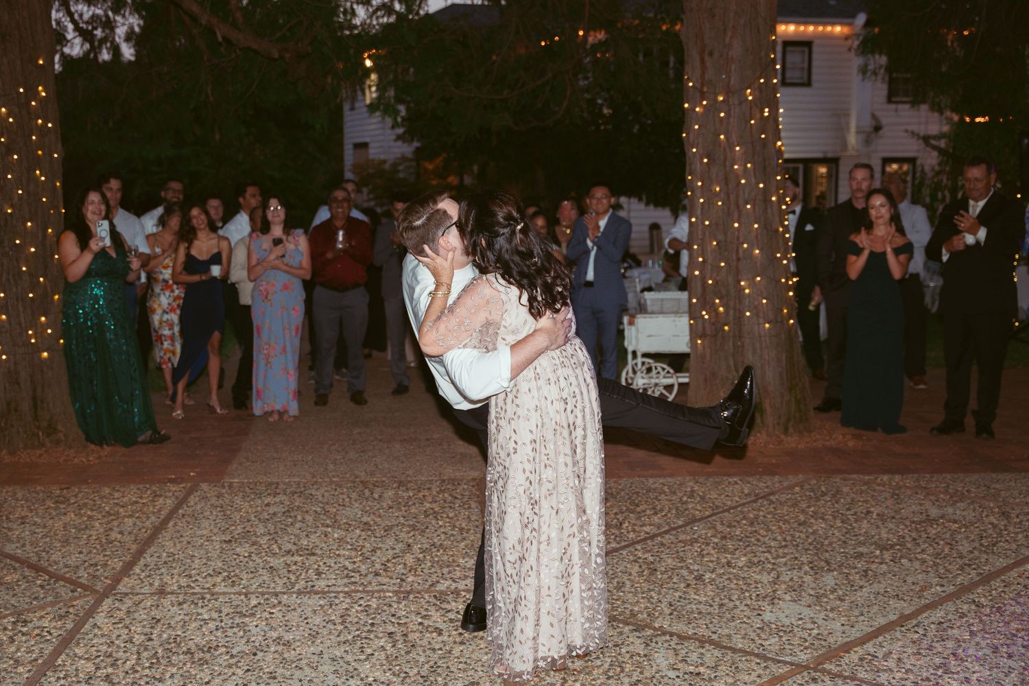 Wedding guests dancing under string lights at an outdoor evening reception.